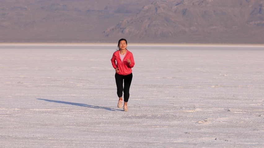 Asian woman jogging across the Bonneville Salt Flats flats in Utah.