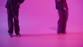 Professional choreographers dancing hip hop on pink neon background. Man and woman dancers showing movements, pair dance, duet. Modern dance school for teenagers.