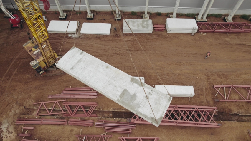 Aerial view. A heavy crane at a construction site is lifting iron concrete slabs.