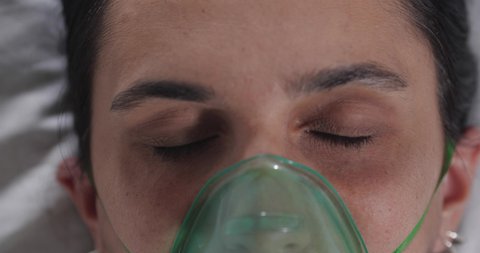 Extreme close-up of a young brunette woman opening her eyes in a hospital bed in an intensive care unit. The patient comes out of a coma or wakes up after anesthesia.