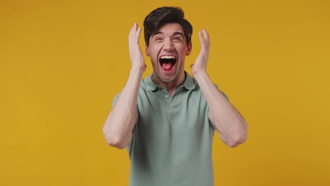 Joyful jubilant surprised shocked young man 20s years old wears blue t-shirt say wow omg what spreading hands doing winner gesture put arms on face screech isolated on plain yellow background studio