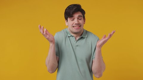 Fun confused awkward confused preoccupied shy shamed young man 20s years old wear blue t-shirt look camera spreading hands say oops ouch oh omg i am so sorry isolated on plain yellow background studio