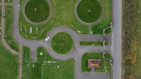 white car driving on roundabout circle in green field with circular patterns at Willow cemetery at Canvey Island in Essex UK. Drone aerial top down view