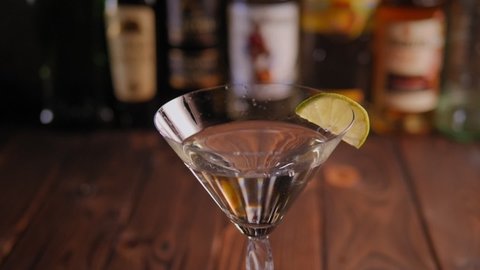 Close-up of a cool cocktail with vermouth and vodka with lime stands on a the background of a bar with bottles.