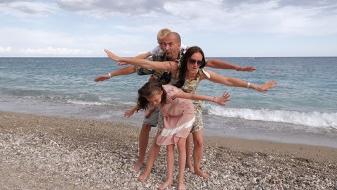 A happy family is having fun on the beach by the sea, they put their hands on the sides together and pretend to fly.