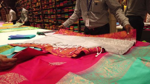Chennai, India - October 17th 2021: Men Cloth seller showing Saree to the customers in a textile shop during diwali festival and family enjoying to purchasing latest traditional Indian clothes.