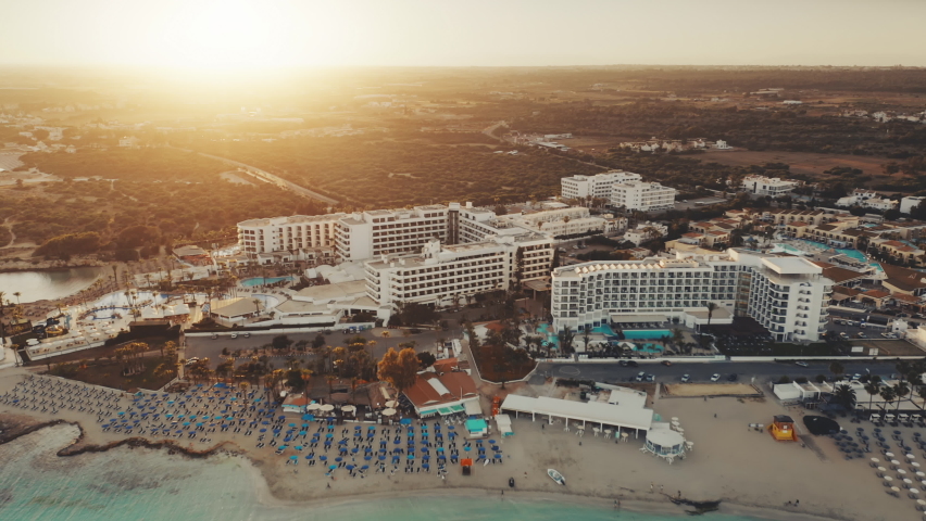 Aerial view of Mediterranean coastline in the sunset. Turquoise crystal water on Nissi Beach, Ayia Napa, Cyprus. Hotels resort complex on the first line. Travel destination landscape. Summer vacation.