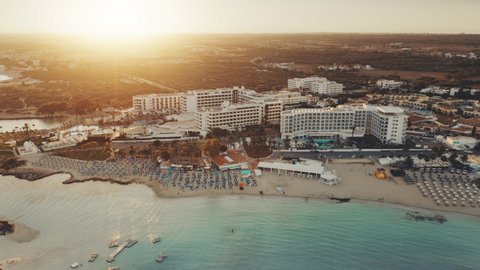 Aerial view of Mediterranean coastline in the sunset. Turquoise crystal water on Nissi Beach, Ayia Napa, Cyprus. Hotels resort complex on the first line. Travel destination landscape. Summer vacation.