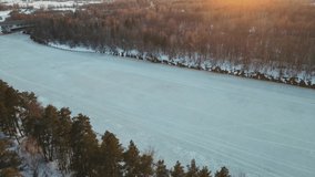 Fantastic winter landscape with frozen river at sunset, aerial view. The ground is covered with white snow. Video, footage, splash screen, intro, presentation, copy space. UHD 4K.