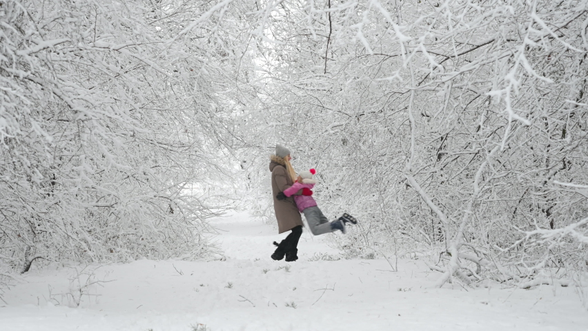 Happy mom plays with her daughter in a beautiful winter park. Family walks outdoors in cold winter. | Shutterstock HD Video #1082684686