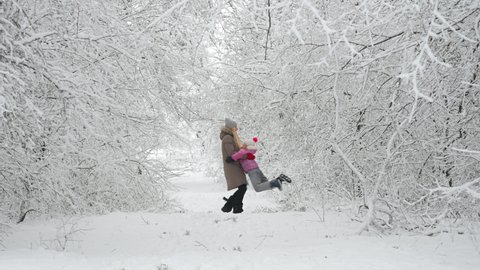 Happy mom plays with her daughter in a beautiful winter park. Family walks outdoors in cold winter.