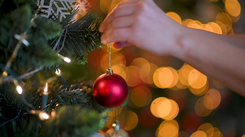 Decorating a Christmas tree. Female hands decorating christmas tree with red baubles against a background of bright colorful garlands