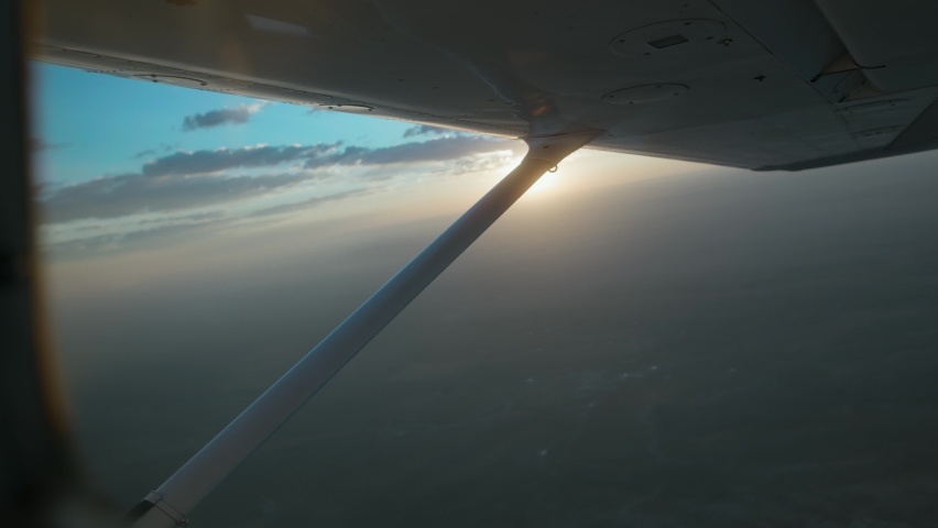 Small Censsna plane flying at 10,000 feet during sunrise. Cinematic sun flares through the hazy morning sky. Royalty-Free Stock Footage #1082685127