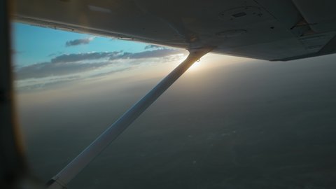 Small Censsna plane flying at 10,000 feet during sunrise. Cinematic sun flares through the hazy morning sky.