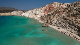 Aerial drone video of iconic volcanic white chalk sandy organised with sun beds and umbrellas beach of Firiplaka with turquoise clear sea and rocky colour formations, Milos island, Cyclades, Greece