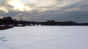 Aerial flying up on frozen wintery river covered in snow with scenic epic cloudy sky in winter. Fast moving clouds in sunset cold sky