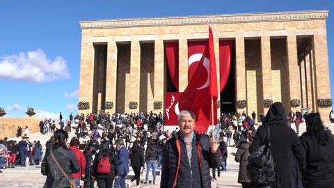 Ankara, Turkey - November 10 2021: The man waving the Turkish flag in his hand and Ataturk's tomb -Anitkabir- in the background with many visitors. 