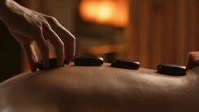 Young woman having hot stone massage in spa salon. Masseur putting stones on back. Close-up of female relaxing on massage table in slow motion. Body relaxation and skin care concept. Evening light - Powered by Shutterstock - Get 15% off with code: PIKWIZARD15