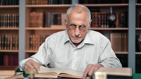 Pensive 70s grandfather focused reading ancient textbook on desk vintage library searching interesting information. Confident elderly man learning educational retro paper book enjoying favorite hobby