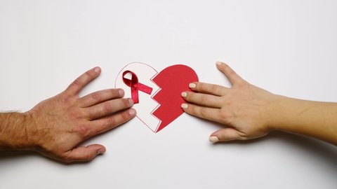 Unfocused video of the reunion of a broken heart of two halves with a red ribbon loop. Symbol World AIDS Awareness Day. Partner's support and assistance. Human rights