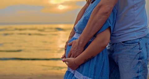 Close-up, male hands carefully touch the tummy of a pregnant woman, fondly stroking it. Man and a pregnant woman are standing on the shore at sunset, waiting for the baby. 4k, ProRes