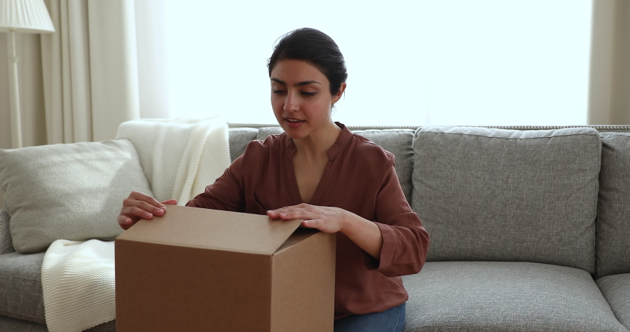 Awaited shipment. Glad Indian female addressee get big parcel box by mail courier service unpack delivery look inside. Curious young lady unbox cardboard container with consumer goods purchased online | Shutterstock HD Video #1082693143