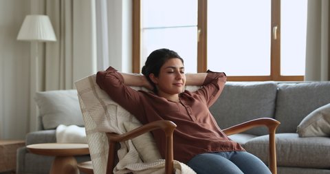 Relax with closed eyes. Serene young Indian female recline in cozy chair take comfy pose chill lounge do nothing in living room. Calm female dream nap in armchair enjoy peace of mind breath fresh air