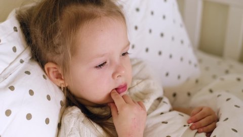 Sick one-year-old child lies in bed and coughs violently, covering her mouth with his hand during an attack. Children's seasonal viral and infectious diseases. Covid 19 quarantine