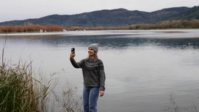 Woman making selfie and a video call showing beautiful views of the lake and bow tie. Vacation vacation trip on the weekend. Happy adventure activity. Beautiful place on the calm water pond at sunset.