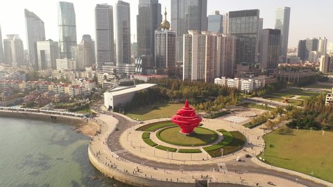 November 21, 2021 - Qingdao, China: May Fourth Wind sculpture in May Fourth Square. Skyscrapers and sun in the background