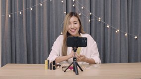 Beautiful Asian female beauty blogger influencer makeup artist recording on smartphone educational tutorial video of cosmetics apply to a subscriber on social media.