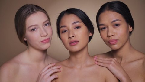 Closeup of three attractive healthy looking young multiethnic women with bare shoulders posing and smiling to camera. Diverse female beauty, skincare for different skin type and smooth complexion