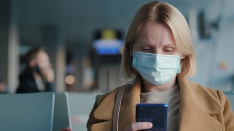 A passenger wearing a mask in the airport lounge. Uses a smartphone