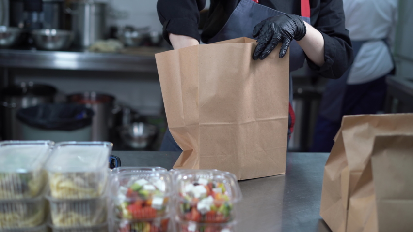 The chef prepares the food in the restaurant and packs it. Disposable food and kraft paper bag ready to ship. | Shutterstock HD Video #1082717785