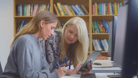 Female university or college student working at computer in library being helped by tutor holding digital tablet- shot in slow motion - Powered by Shutterstock - Get 15% off with code: PIKWIZARD15