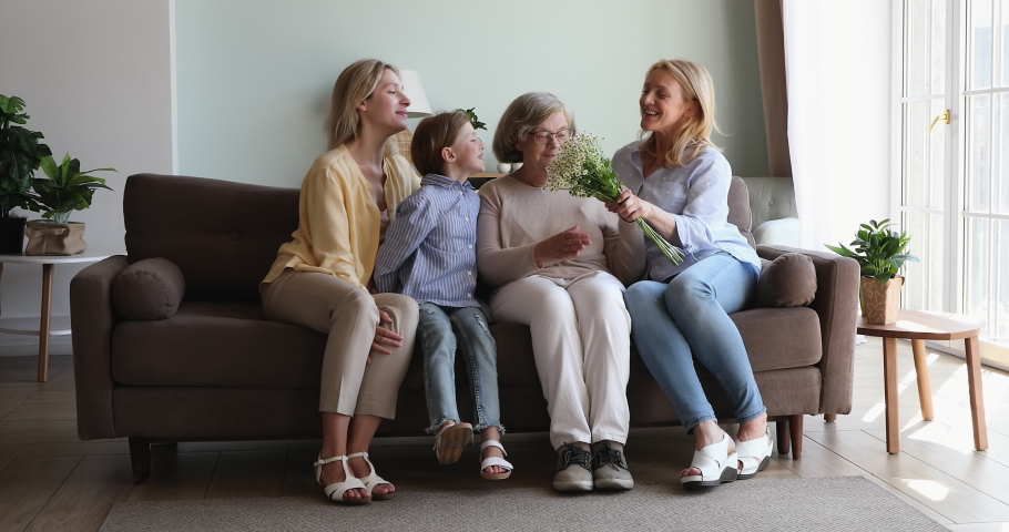 Small girl great grandkid adult granddaughter aged daughter hug senior mom granny great grandma wish happy birthday. Female dynasty of 3 relatives give card flowers to senior lady in family on March 8 Royalty-Free Stock Footage #1082724241