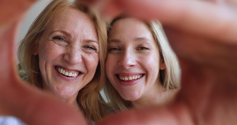 Smiling faces loving mature mother young daughter posing for selfie video portrait making heart of fingers. Happy female grownup child join hands in love symbol with aged mom look at camera. Close up