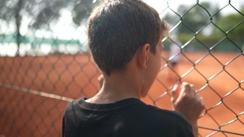 Child leaning on tennis match fence watching sport game