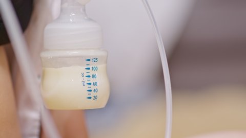 Mother using breast milk pump for baby.Close up Milk from breast pump dropping into milk bottle storage for baby newborn.