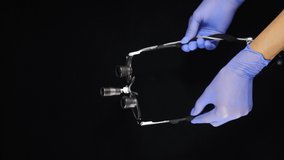 Hands in blue gloves holding binoculars on black background. Modern dentistry with actual equipment. Vertical footage. Dentist glasses binocular and magnification. 4 k video
