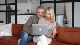 Middle-aged couple in love using laptop sitting on the couch at home. Cheerful senior couple watching movie together, smiling and hugging at cozy living room, web surfing and spends time online - Powered by Shutterstock - Get 15% off with code: PIKWIZARD15