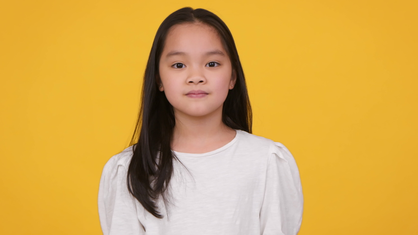 Hmm, let's think. Studio portrait of cute thoughtful little asian girl contempaining about idea, touching her chin, orange background, slow motion Royalty-Free Stock Footage #1082735518