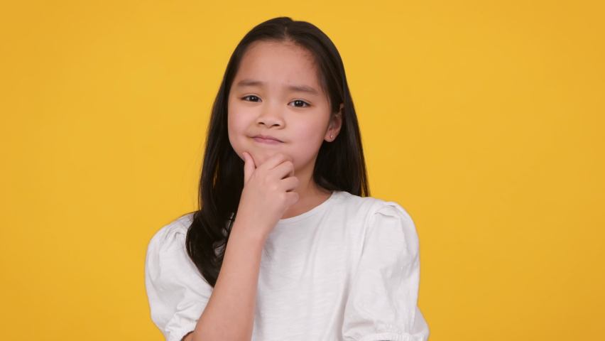Hmm, let's think. Studio portrait of cute thoughtful little asian girl contempaining about idea, touching her chin, orange background, slow motion Royalty-Free Stock Footage #1082735518
