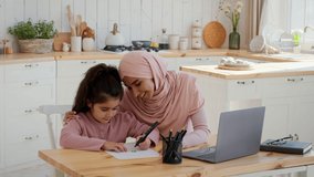 Happy Islamic Mother And Little Daughter Drawing Together Bonding And Having Fun Sitting In Modern Kitchen At Home. Family Weekend Leisure And Pastime. Slow Motion