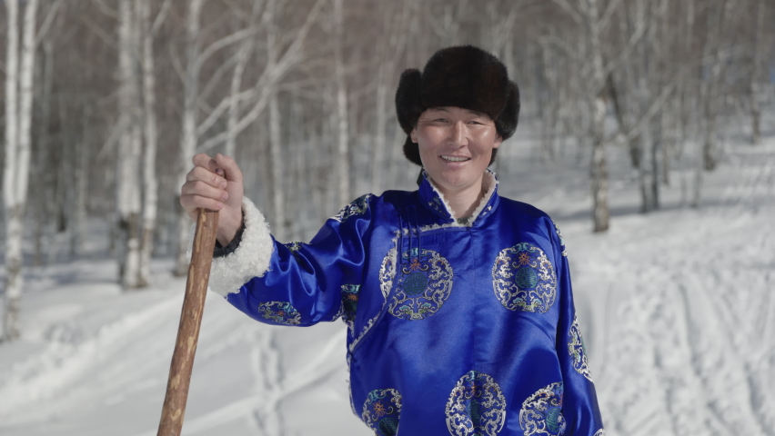 Confident Mongolian man dressed in traditional deel standing outside in snow.