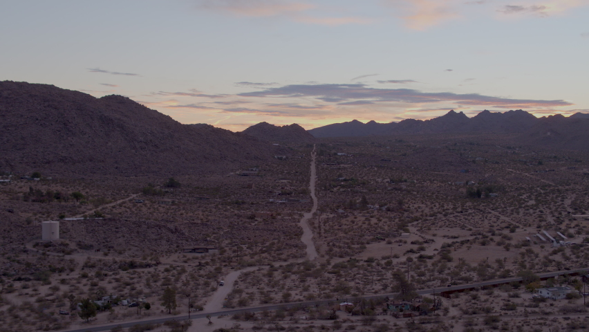 Aerial push towards and over lonely dirt road heading towards the hills of Joshua Tree National Park in California on a beautiful evening at sunset.
