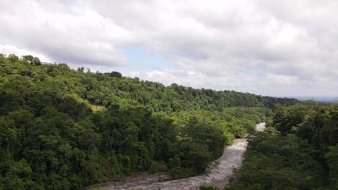4k aerial footage of backwards flying drone passing high trees very closely. Fast and heavy clouds above beautiful lush rainforests. Brown river meandering underneath. Eco tourism concepts in ultra HD