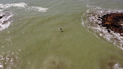 Man balancing on slackline over ocean waters. Aerial top-down circling