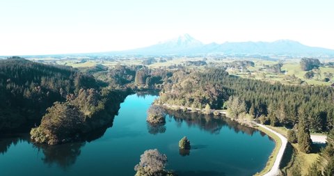 Aerial over the lake towards a snow capped volcano with intense morning sun