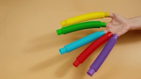 Group of multicolored rainbow toy pop it tube in hand on beige background, trend toy for the development of fine motor skills of hands, anti stress crackling tube.
